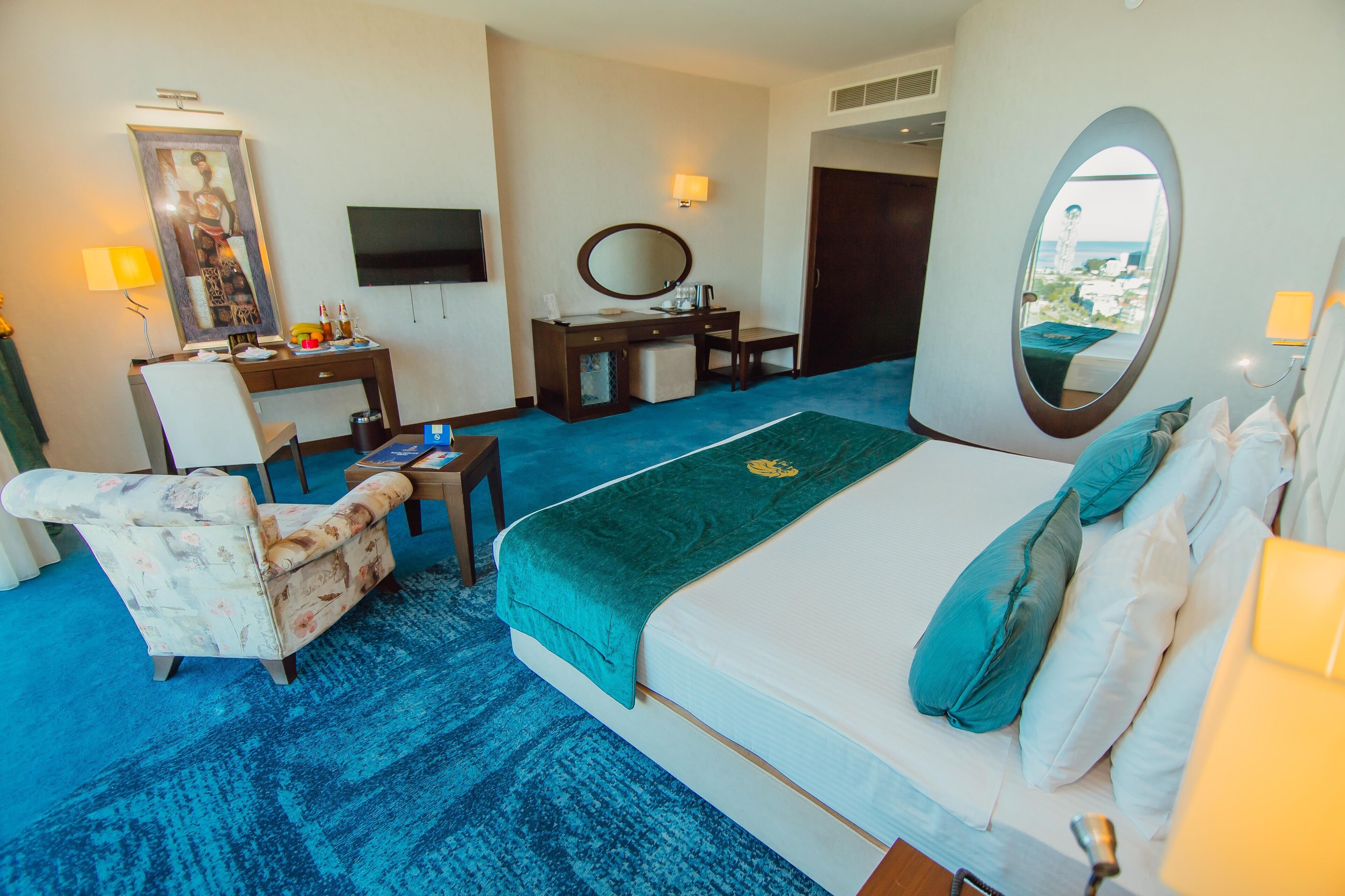 A hotel room with a bed, a desk, a chair, a television, and a large mirror.