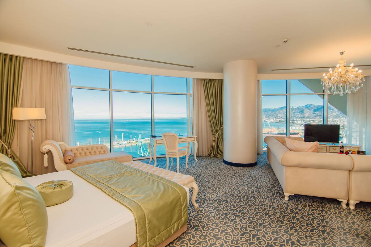 Ein Hotelzimmer mit Bett, Schreibtisch, Sofa und einem großen Fenster mit Blick auf das Meer.