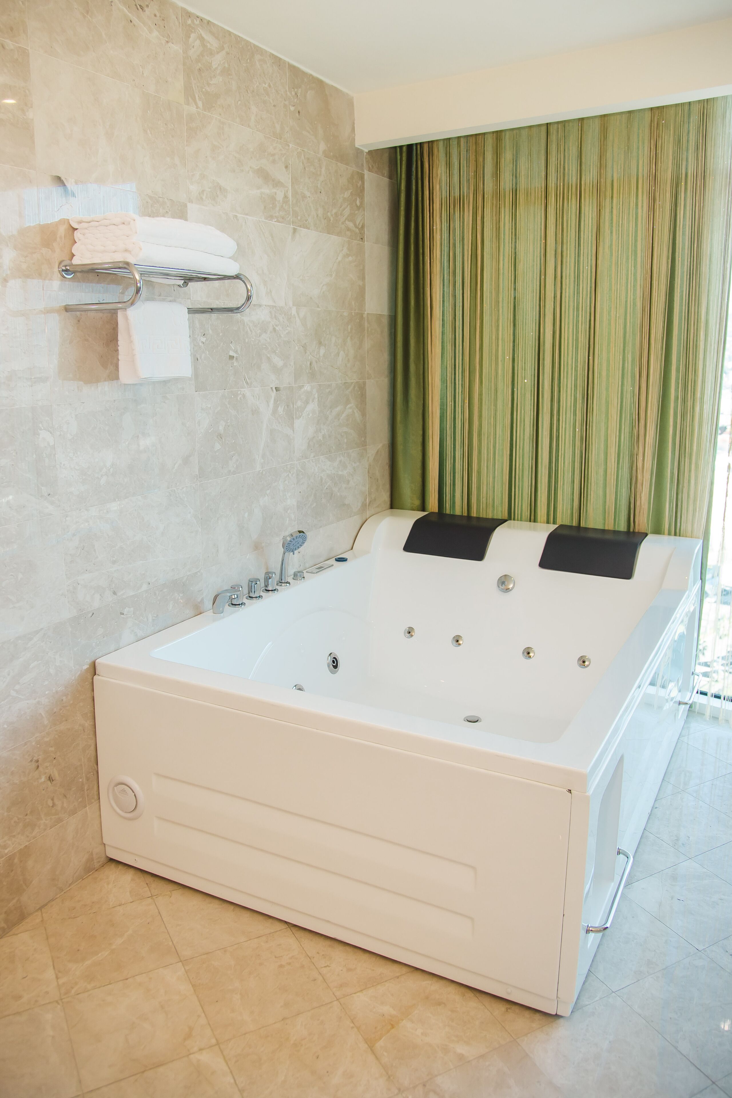 A large, white bathtub with multiple jets, a towel rack with folded towels, and a green curtain.