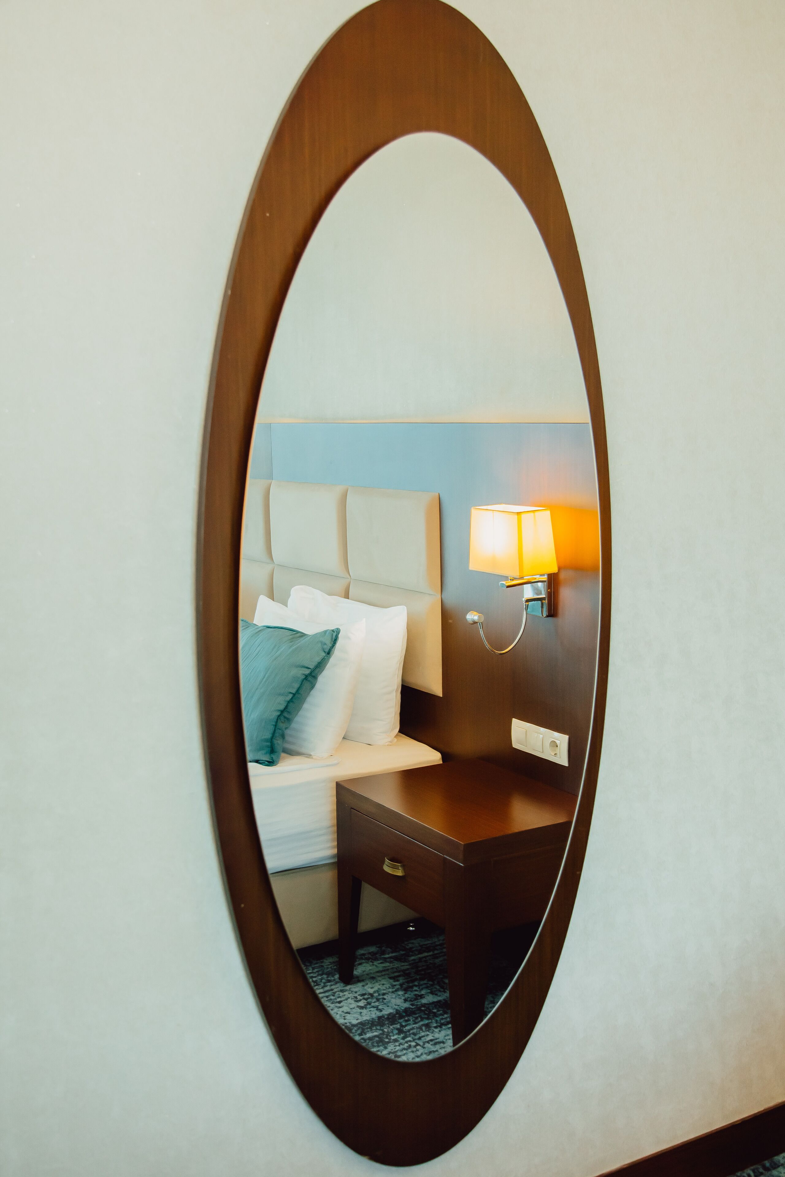 A hotel room with a bed, a nightstand, a lamp, and a mirror.