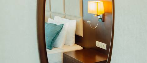 A hotel room with a bed, a nightstand, a lamp, and a mirror.