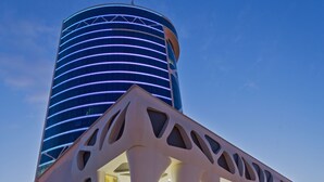 A modern building with a unique architectural design featuring large, white, geometric cutouts and a cylindrical structure with illuminated lines. - JRW Welmond Hotel & Casino Batumi (Batumi)