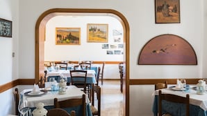 Un espace repas avec des tables préparées pour deux personnes, des œuvres d’art encadrées accrochées aux murs et une vue dégagée sur l’extérieur, visible à travers une arche.