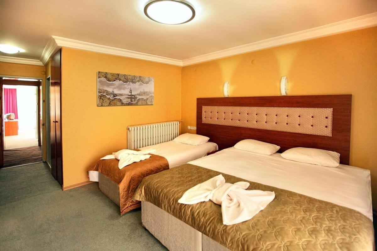 Une chambre d’hôtel avec deux lits, un radiateur, un tableau au mur et une porte donnant sur une autre pièce.