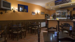 Un restaurante con mobiliario de madera, una zona de bar y un televisor en la pared.