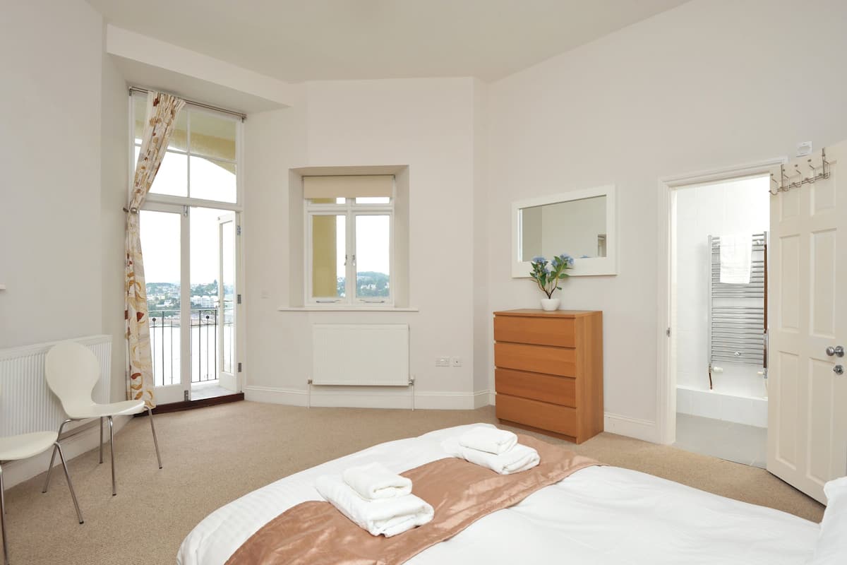 Une chambre à coucher avec un lit, une commode, une chaise, une fenêtre et une porte.
