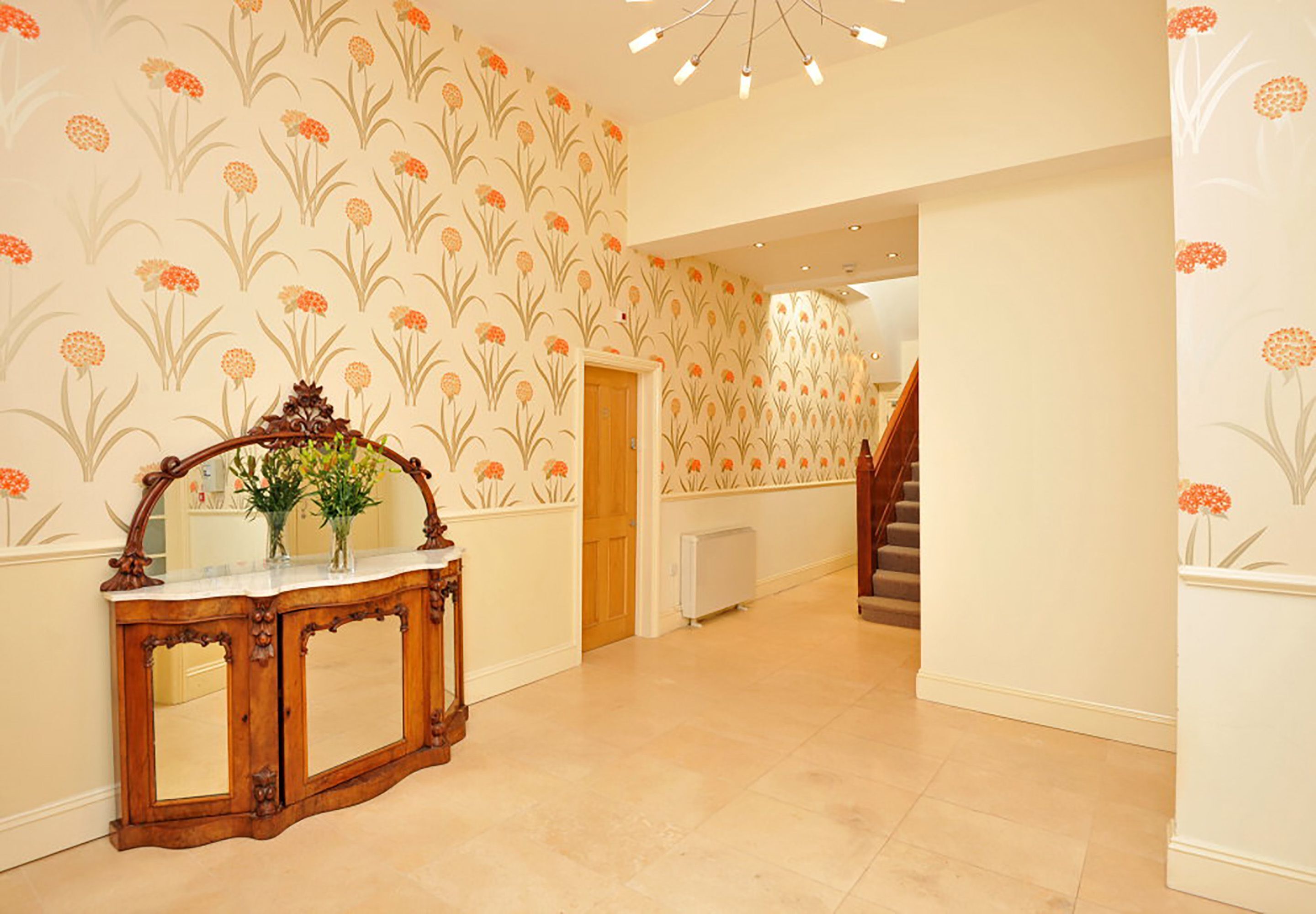 Ein Flur mit blumengemustertem Wandpapier, einem Holzkonsolentisch und einem Spiegel sowie einer Treppe.