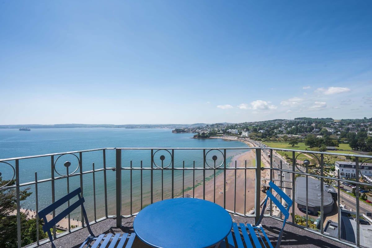 Un balcon avec une table et des chaises donnant sur une plage et la mer.