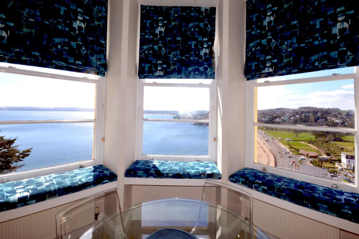 Une baie vitrée avec trois sièges, offrant une vue sur la mer et une ville située au loin.