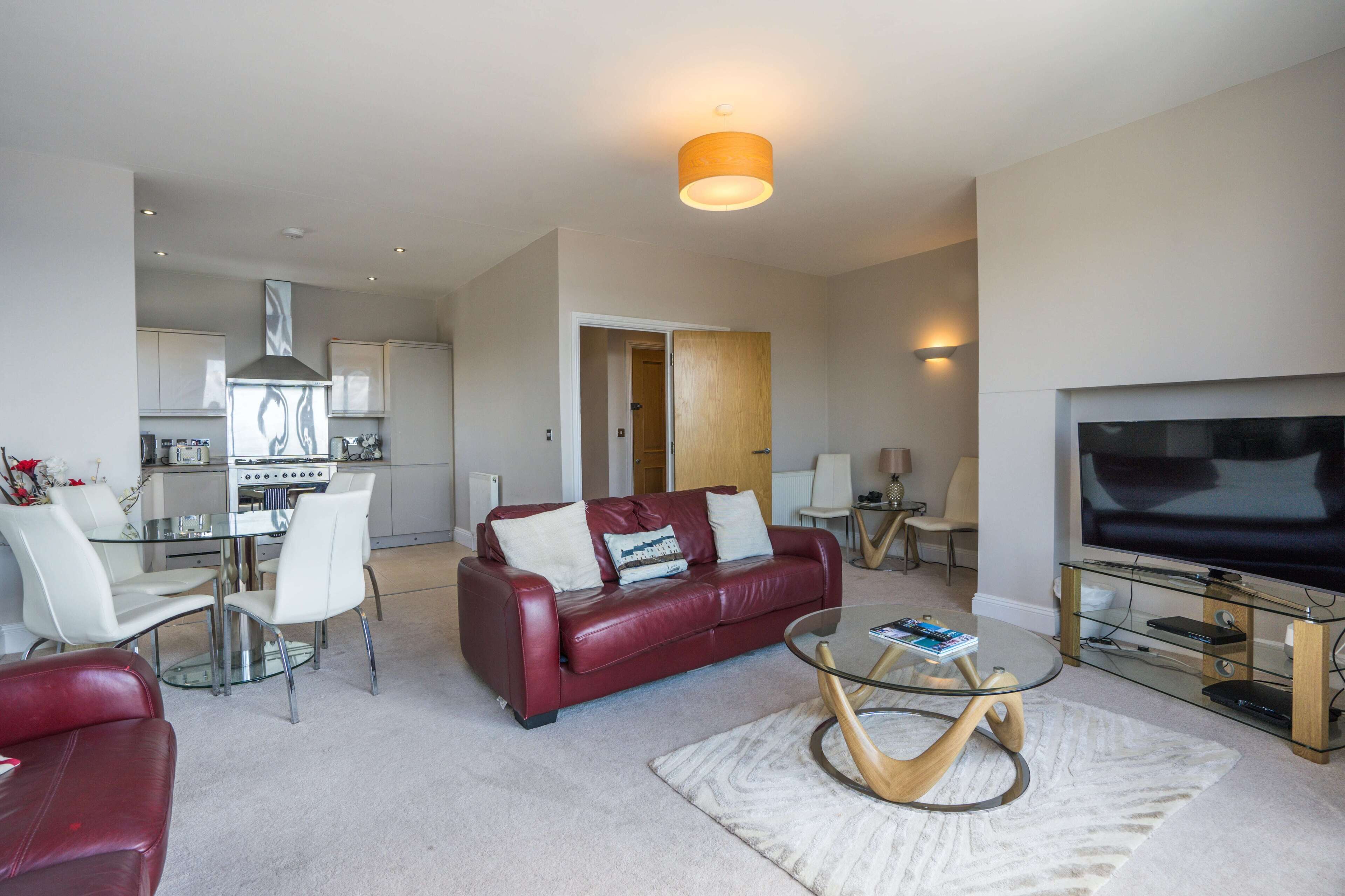 A modern living room with a red leather sofa, a glass coffee table, and a flat-screen TV.