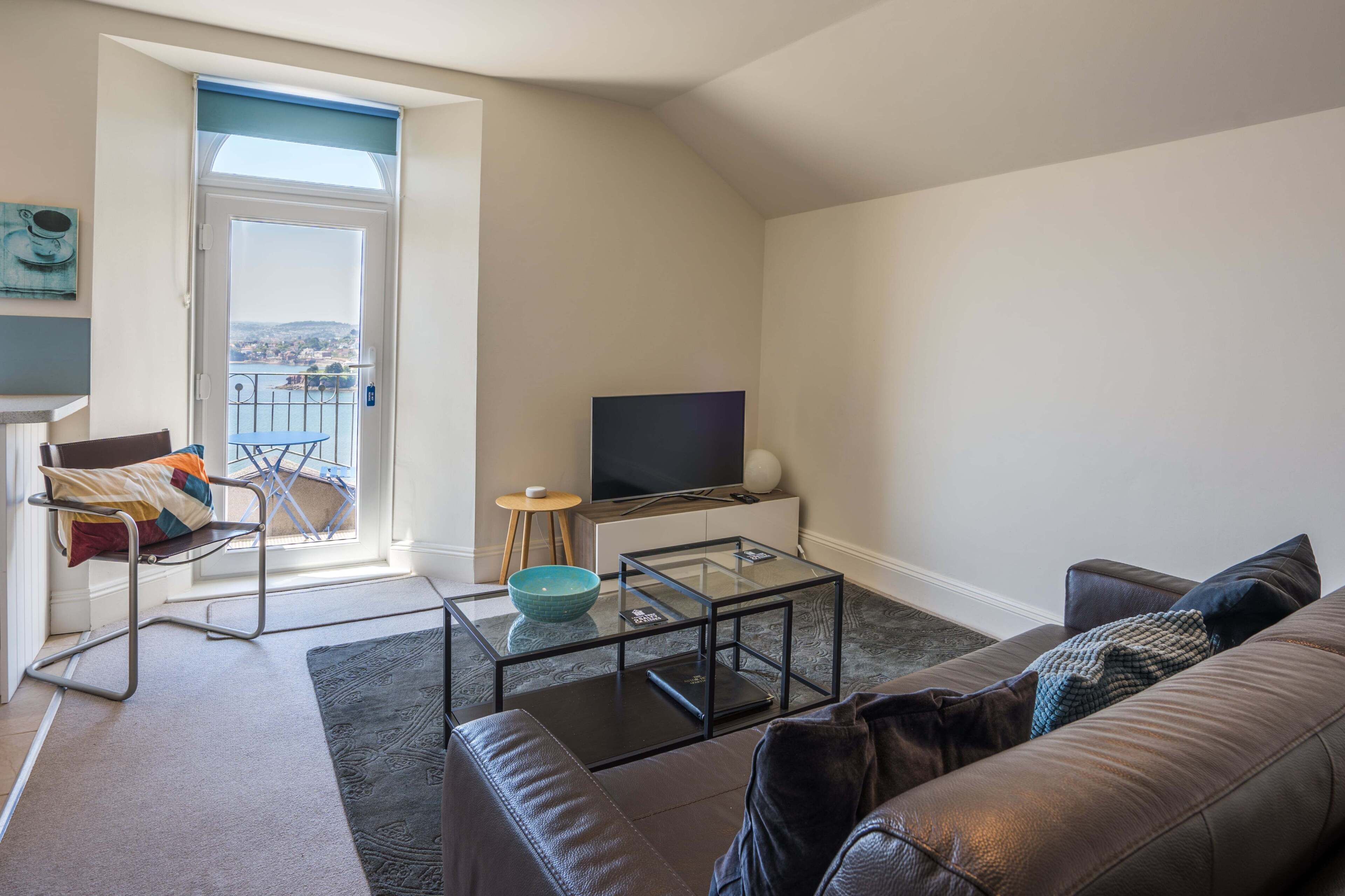 A living room with a sofa, a glass coffee table, a TV, a chair, and a view of a balcony.