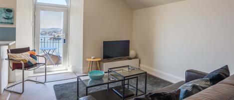 A living room with a sofa, a glass coffee table, a TV, a chair, and a view of a balcony.