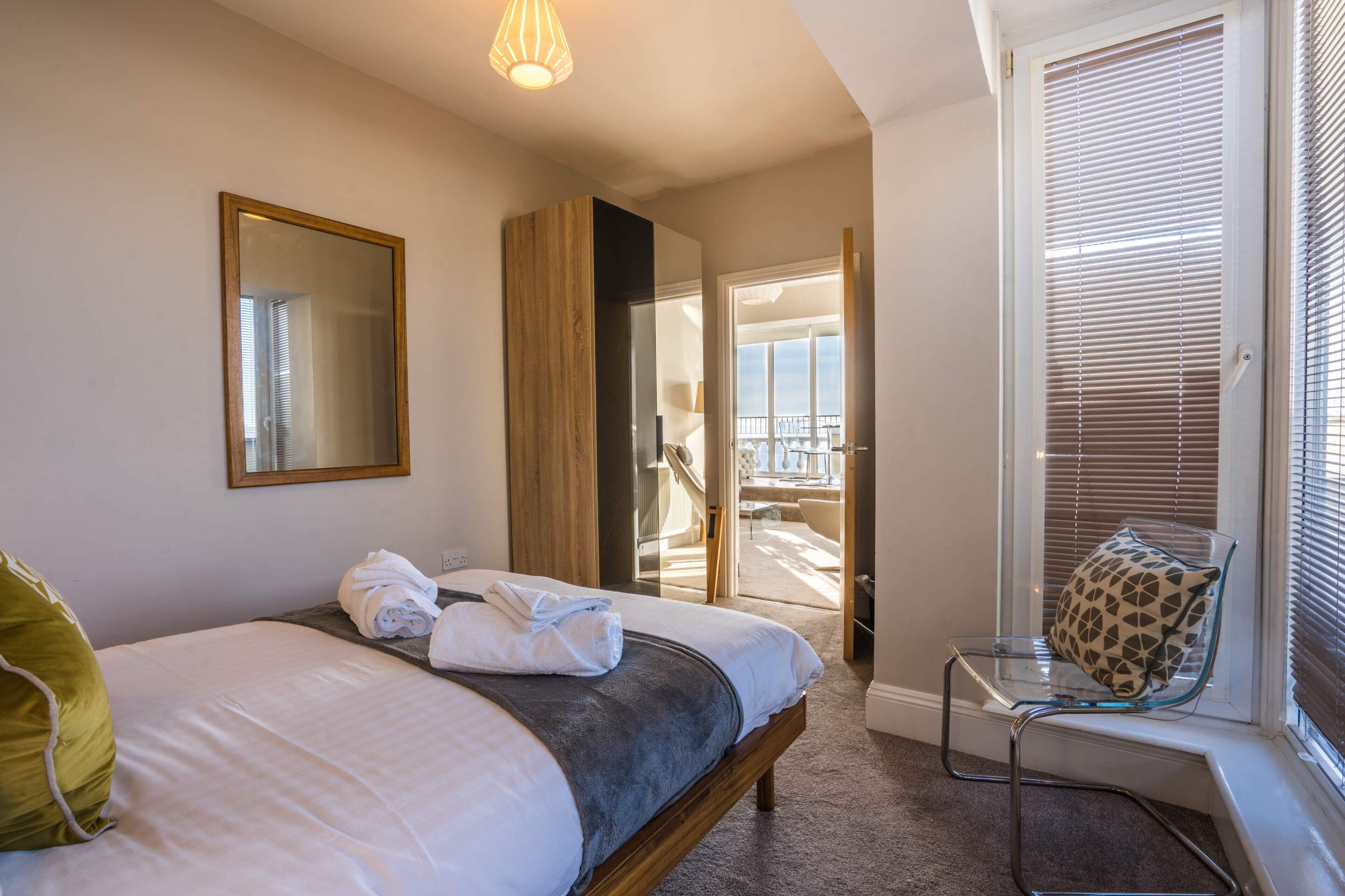 Una habitación de hotel con una cama, una silla, un ventanal con persianas y una puerta que da a un balcón.