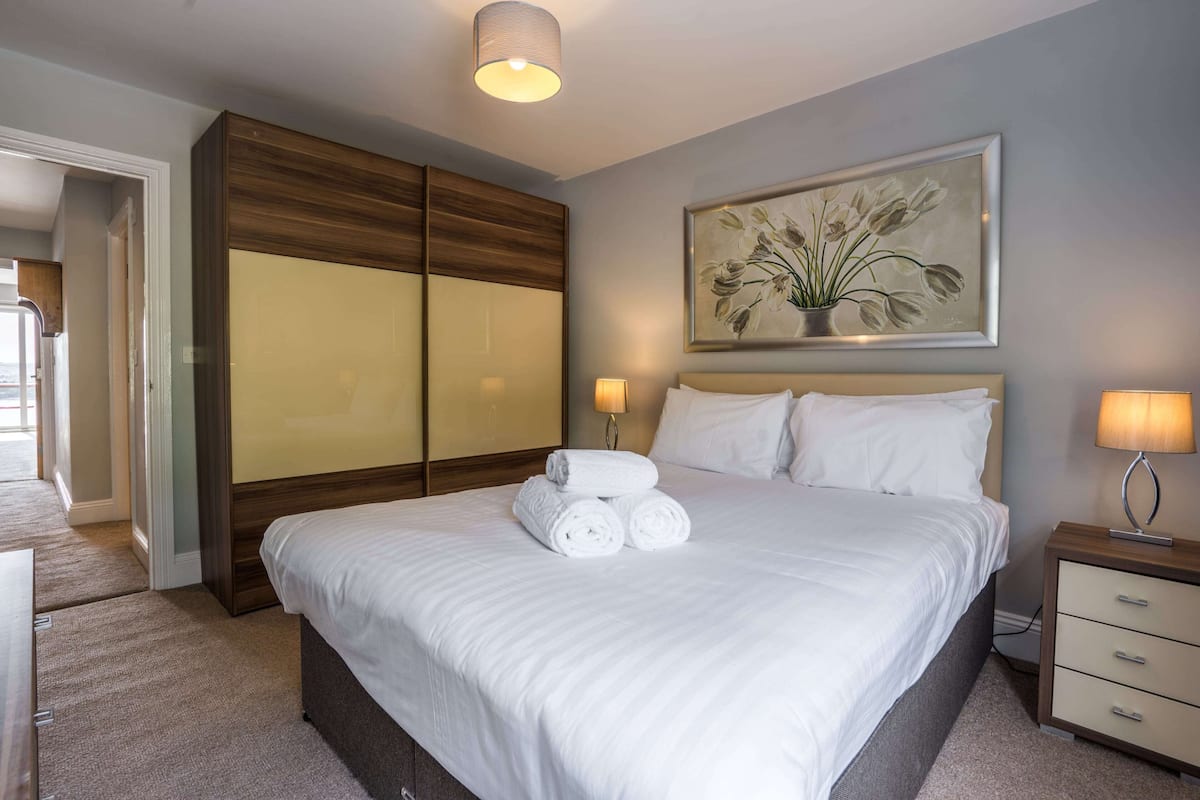 Une chambre d’hôtel avec un grand lit, une armoire en bois, une table de chevet avec une lampe et un tableau au mur.