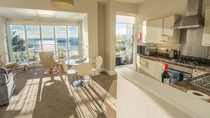 A modern kitchen with a large island, a dining area with a view, and a balcony with a scenic view. - Astor House (Torquay)
