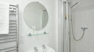 Un baño moderno con cabina de ducha de vidrio, un espejo redondo, un lavabo blanco y un perchero.