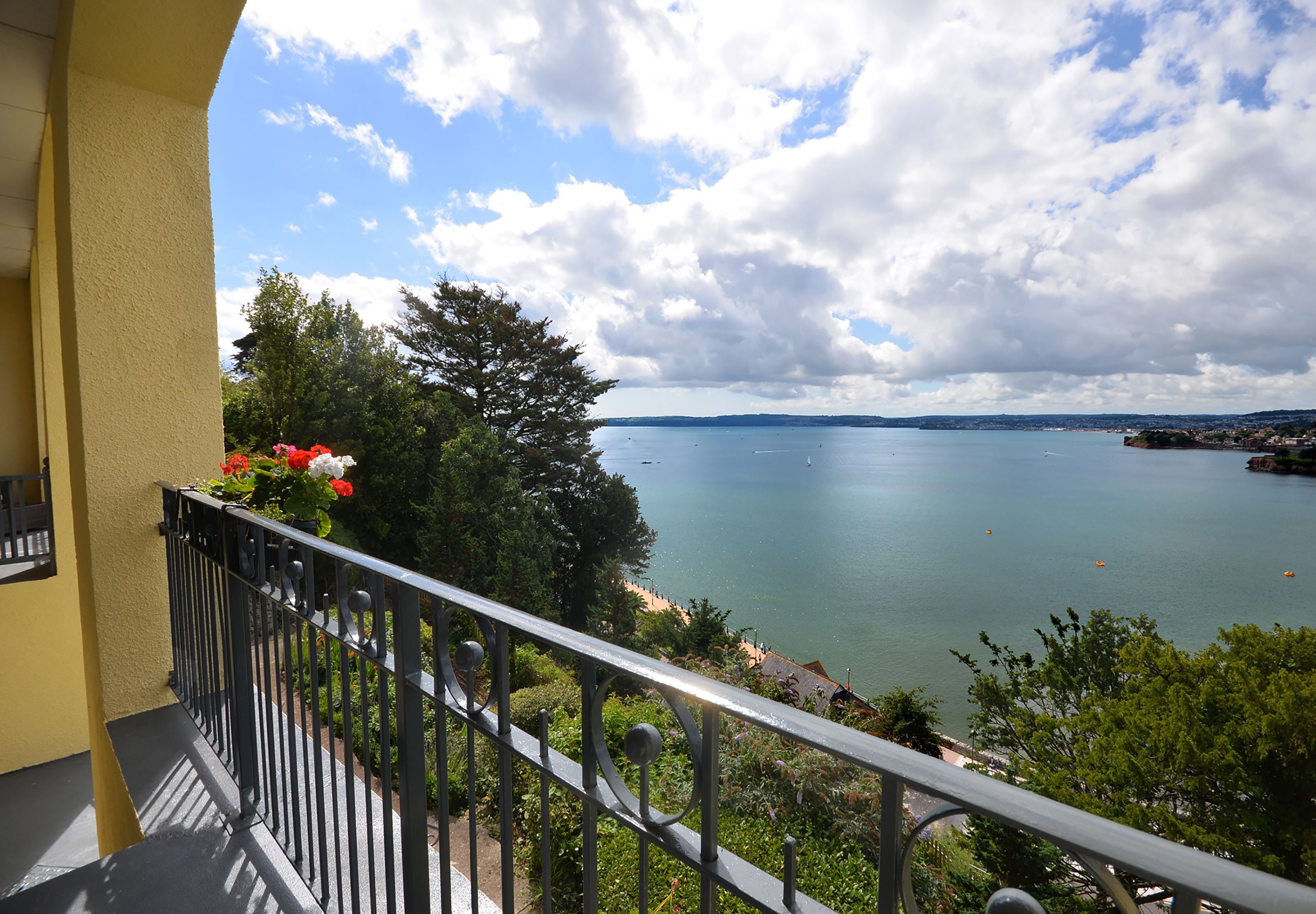 A balcony with a view of a lake, surrounded by greenery and a clear sky.