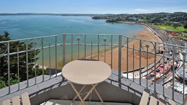 A balcony with a table and chairs overlooking a beach and a coastal town. - Astor House (Torquay)