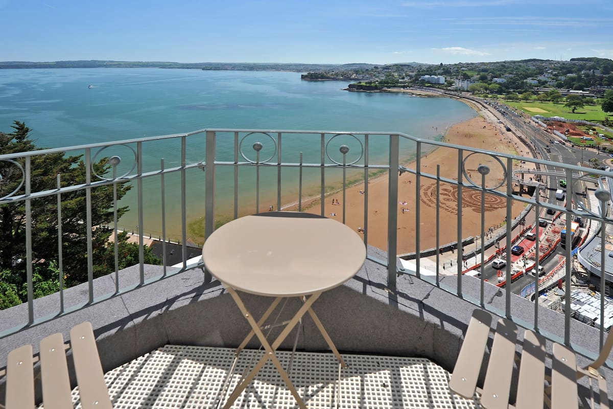 Un balcon avec une table et des chaises donnant sur une plage et une ville côtière.