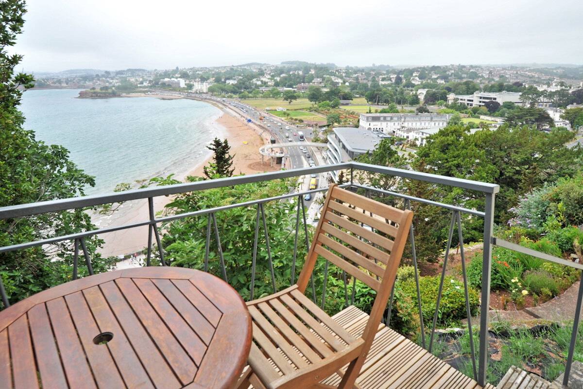 Une terrasse en bois avec une table et une chaise, offrant une vue sur la plage et le paysage urbain.