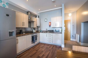 Una cocina moderna con electrodomésticos de acero inoxidable, armarios blancos y piso de madera.