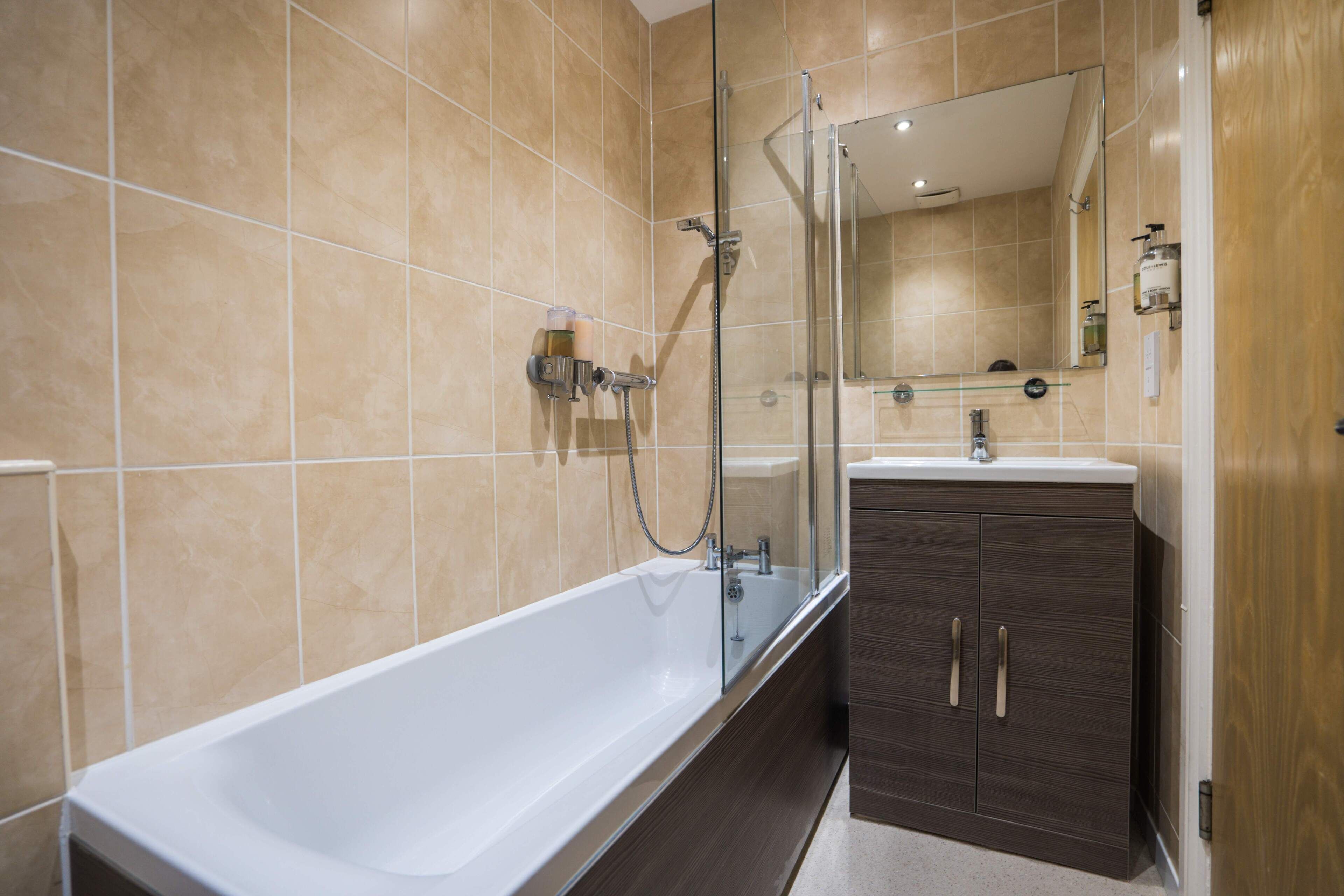 Un bagno moderno con una vasca da bagno ampia, un box doccia in vetro e mobili contenitori in legno scuro.