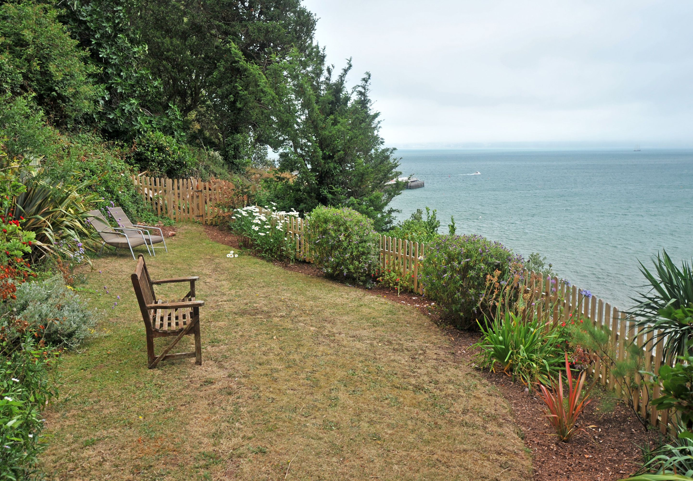 A garden with a wooden chair, a wooden fence, and a view of the sea.