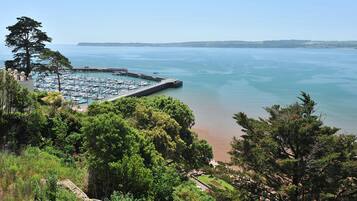 A marina with boats docked, surrounded by lush greenery and a clear view of the sea.
