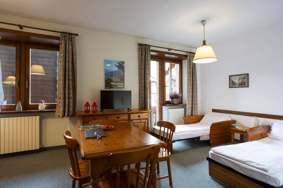 A cozy room with a wooden table, two single beds, a TV, and a window with curtains.