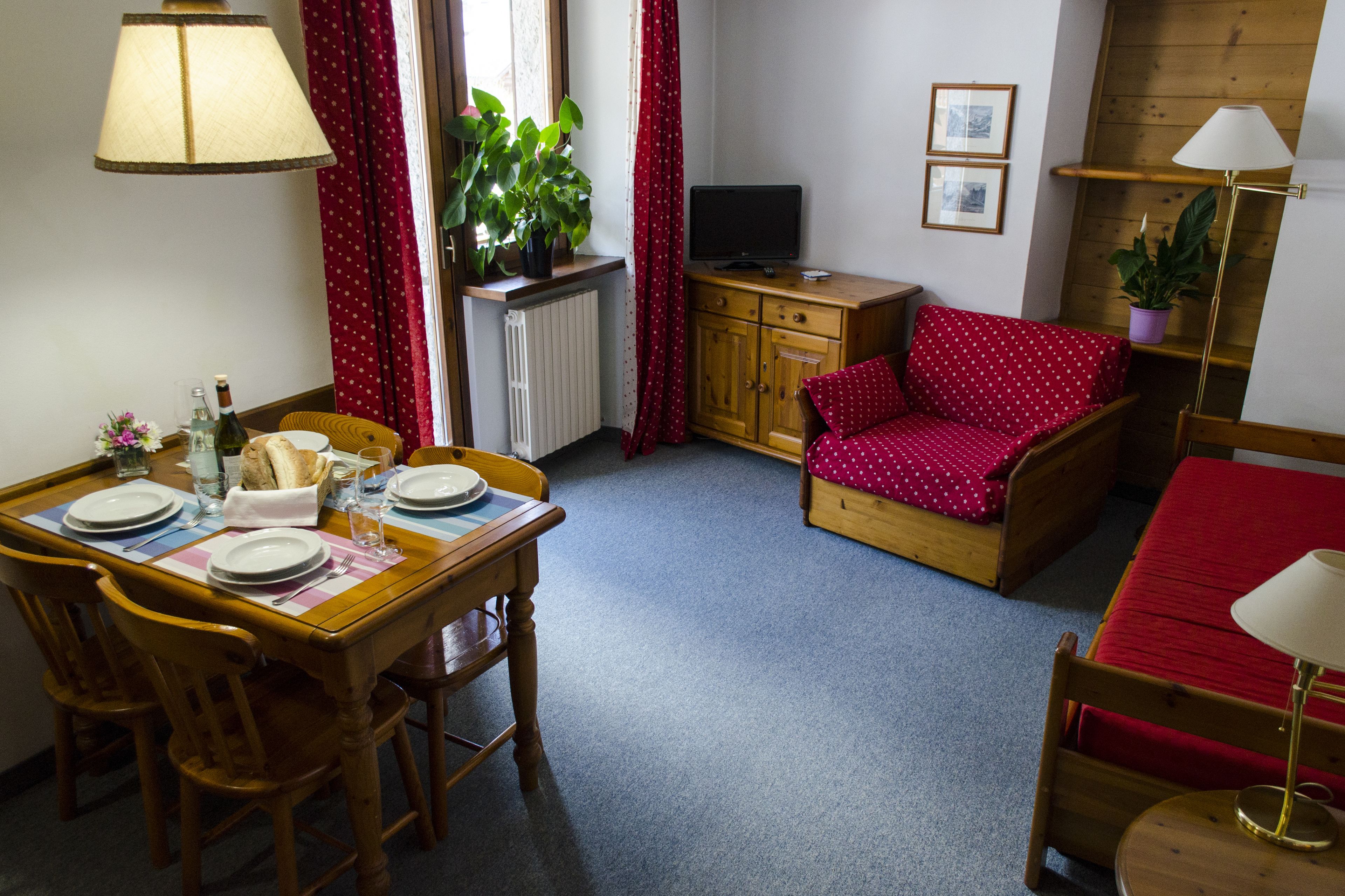 A cozy room with a dining table set for two, a red polka dot sofa, a television, and a plant.