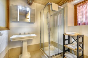 A bathroom with a glass-enclosed shower, a pedestal sink, and a wooden shelf with towels. - Residence Cima Jazzi (Macugnaga)