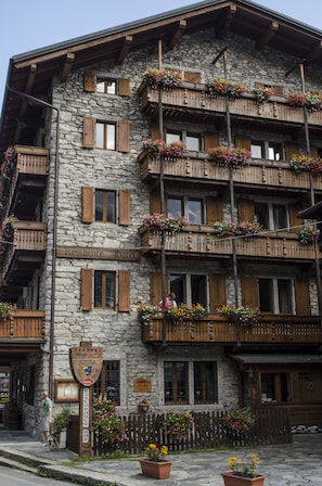 Un edificio de piedra con balcones de madera decorados con flores, un letrero que indica que es un hotel y una cerca de madera al frente.