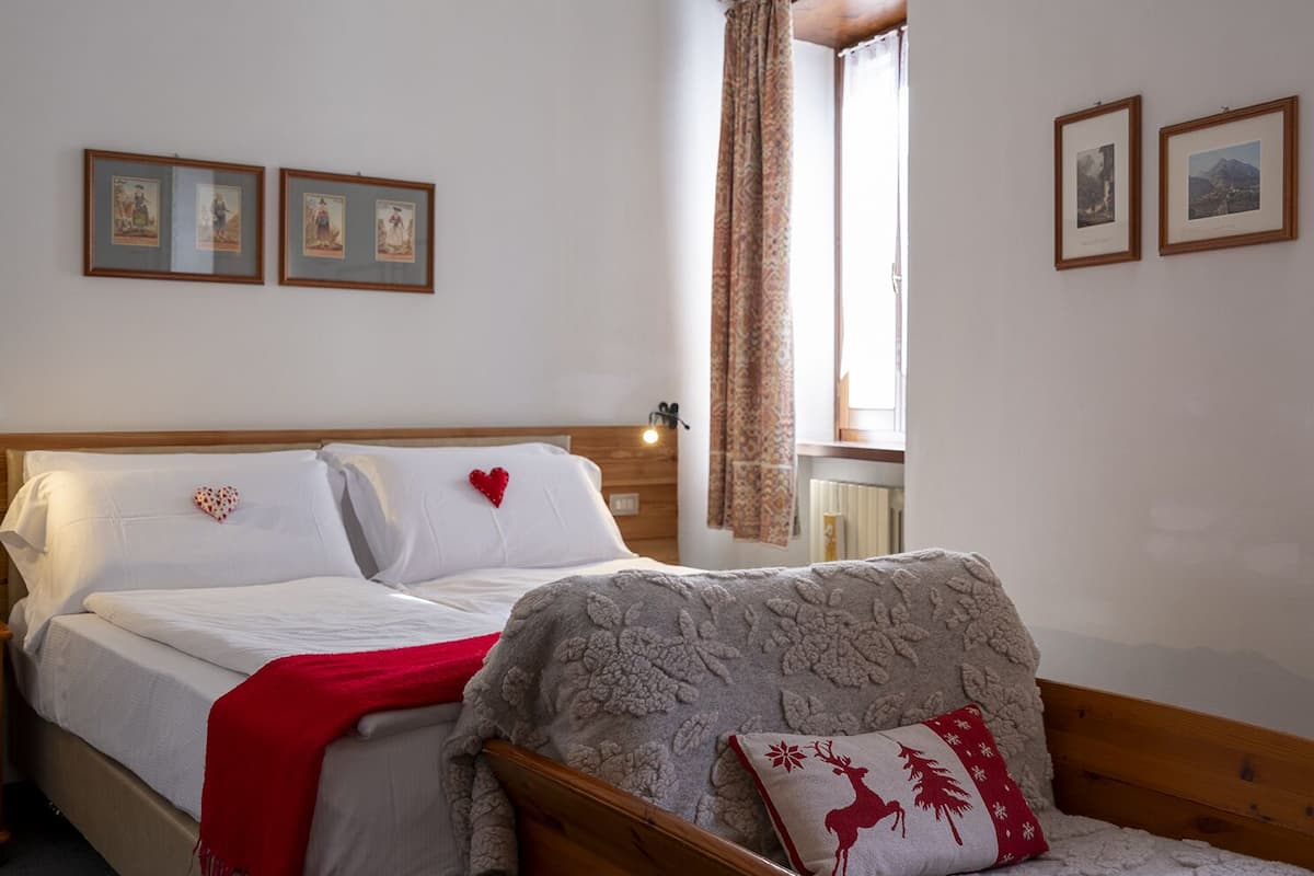 A bedroom with two beds, a window with curtains, and framed pictures on the wall.
