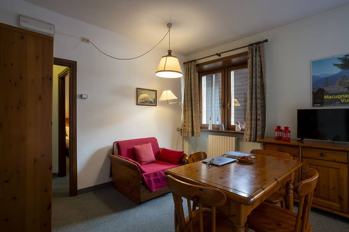 A cozy room with a wooden dining table, a red sofa, and a television.