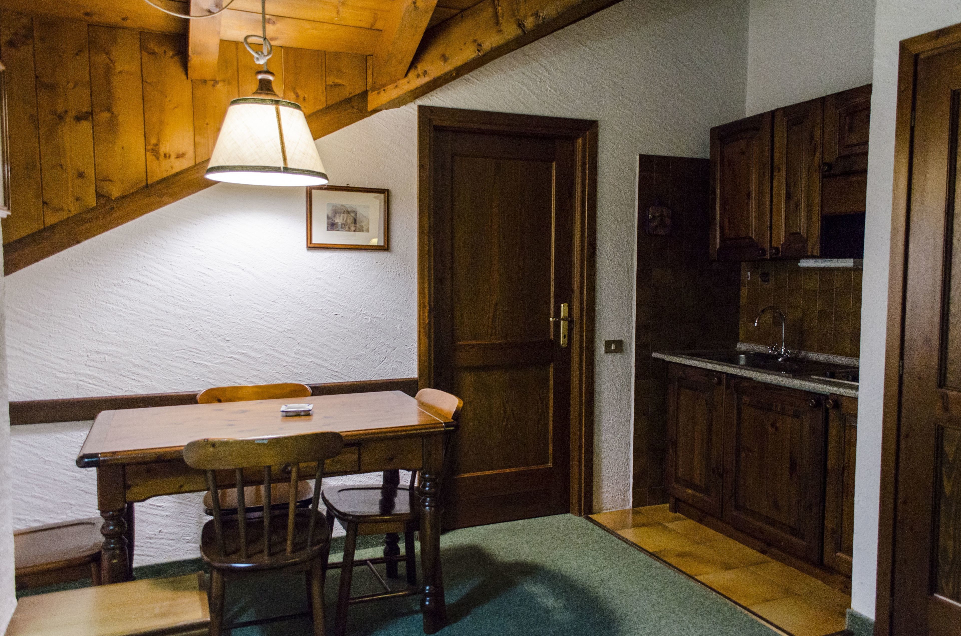 A dining area with a wooden table and chairs, a hanging light fixture, and wooden cabinets in the background.