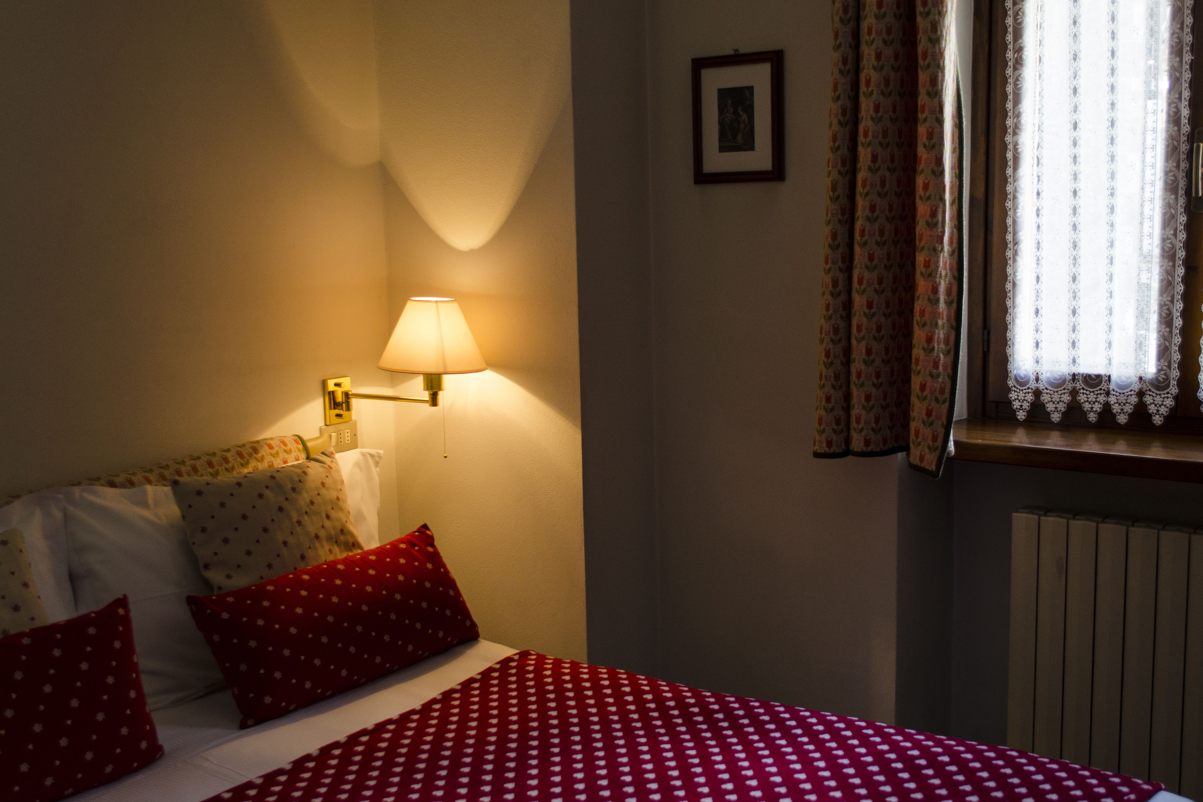 Une chambre d’hôtel avec un lit, une lampe fixée au mur, un tableau encadré et une fenêtre avec des rideaux.