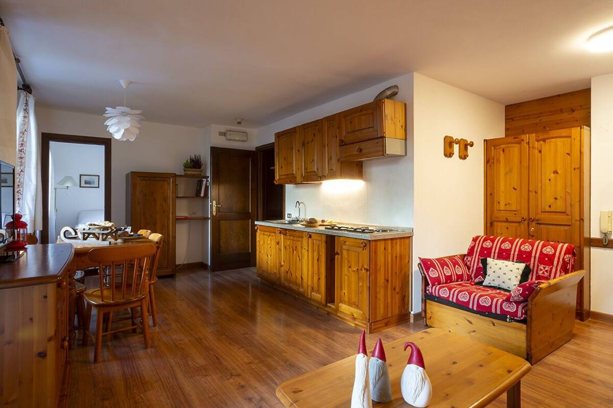 A cozy living room with a wooden sofa, a dining table with chairs, and a kitchen area with wooden cabinets and a countertop.