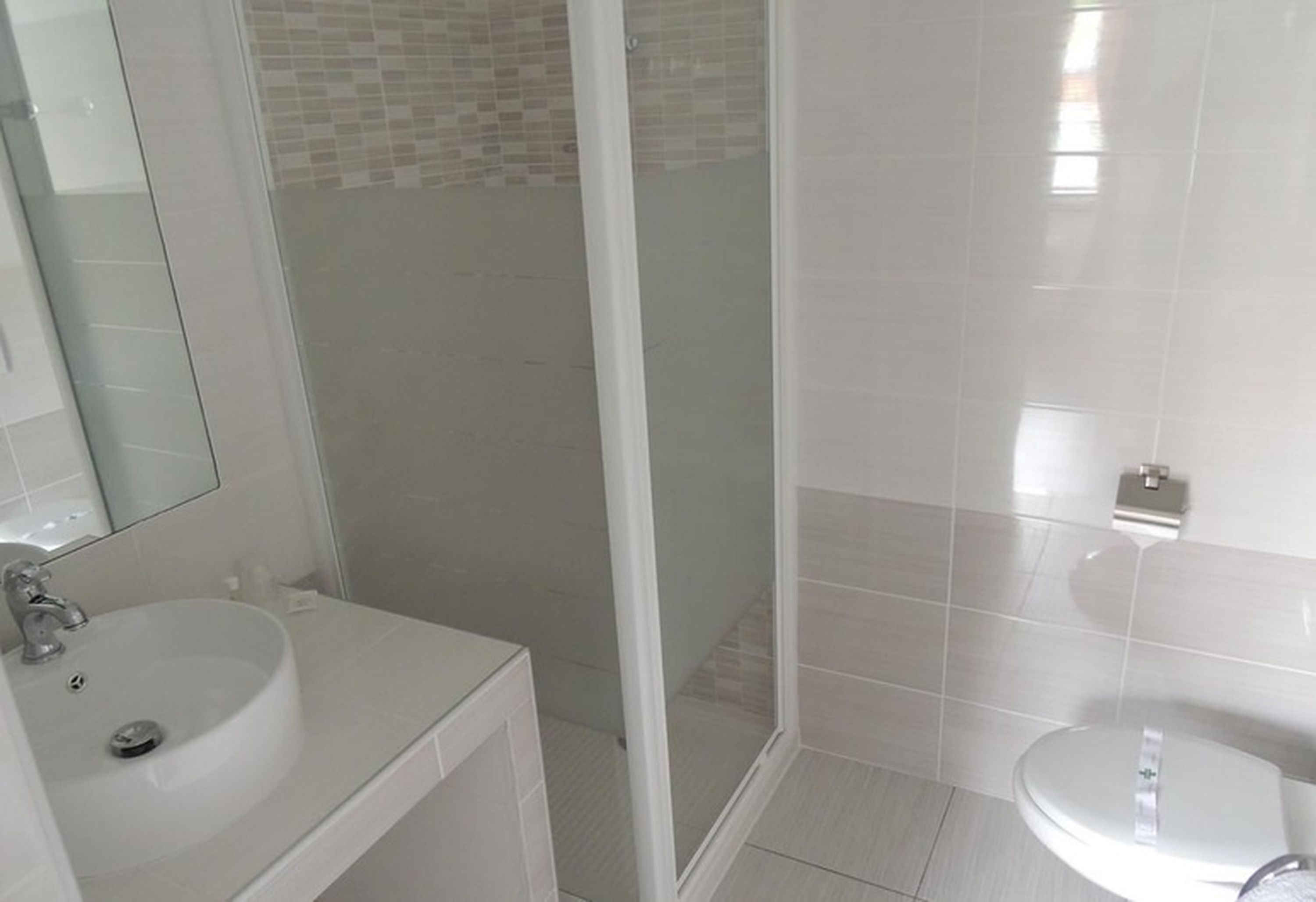 Een badkamer met een witte wastafel, een spiegel, een douchecabine en een toilet.