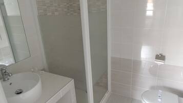Een badkamer met een witte wastafel, een spiegel, een douchecabine en een toilet.