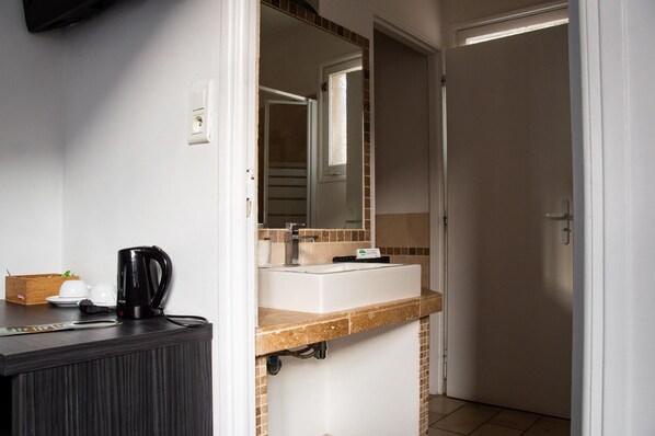 Baño con lavamanos, espejo y cafetera en la encimera.