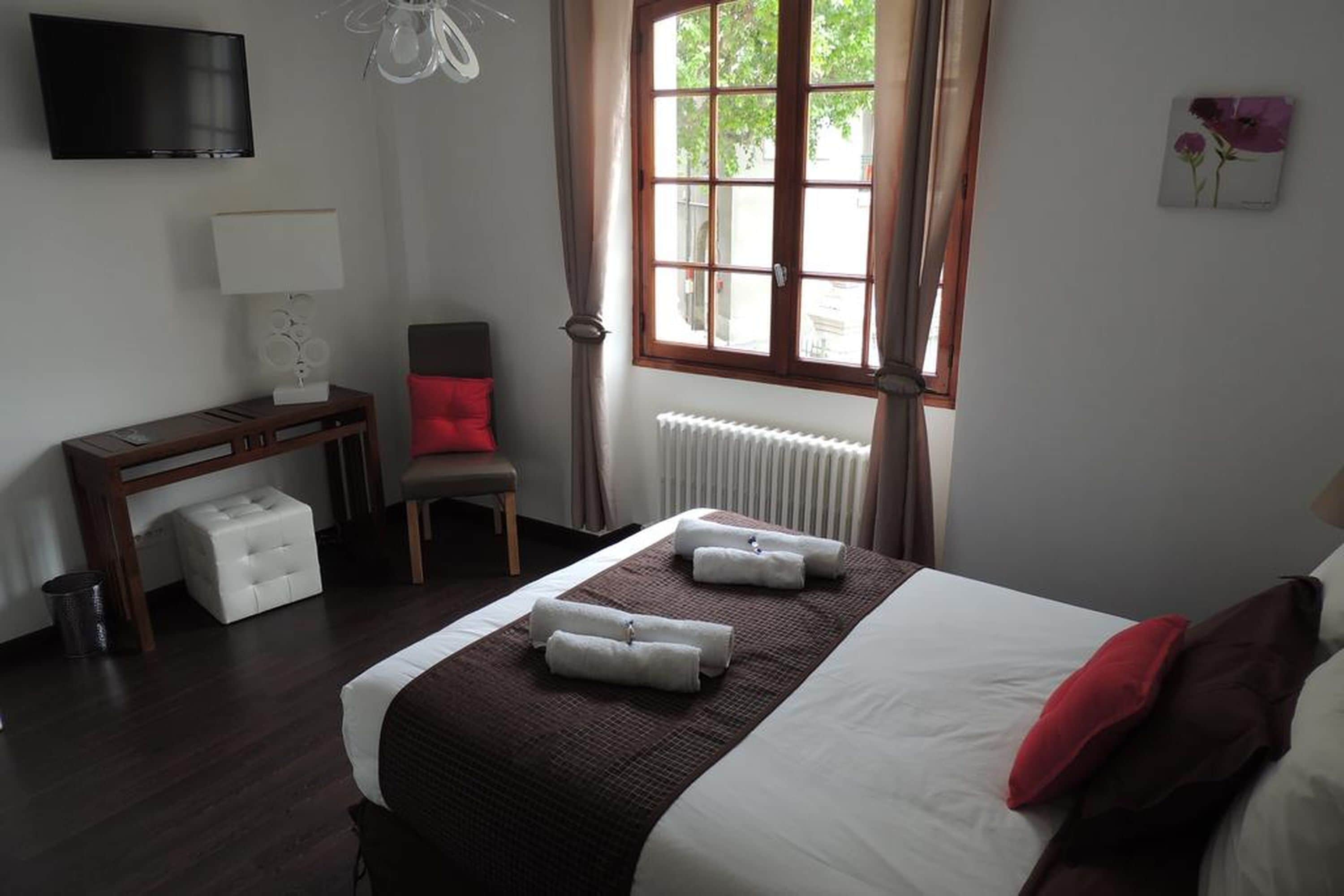 Una habitación de hotel con cama, escritorio, silla, radiador y ventana con cortinas.