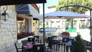 An outdoor dining area with tables and chairs, umbrellas, and a view of a building with a sign that reads "RESTAURANT".