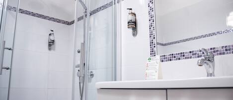 Un baño moderno con cabina de ducha de vidrio, un lavamanos blanco con grifo plateado y un salpicadero de azulejos con un diseño decorativo.