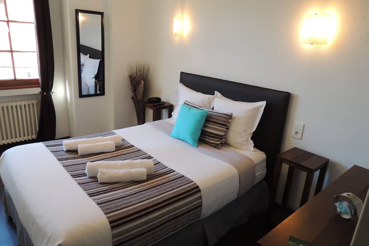 A hotel room with a large bed, a bedside table, a nightstand, a mirror, and wall-mounted lights.