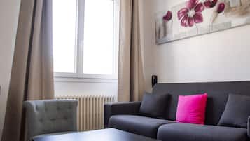 A room with a grey sofa, a black coffee table, and a painting of flowers on the wall.