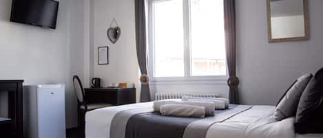 A neatly arranged bedroom with a bed, a desk, a television, and a radiator.