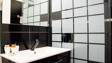 Un baño moderno con un lavamanos blanco, azulejos negros y un espejo grande.