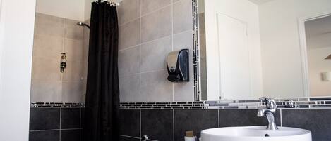 Un baño con un lavamanos blanco, un espejo, una ducha y un perchero para toallas.