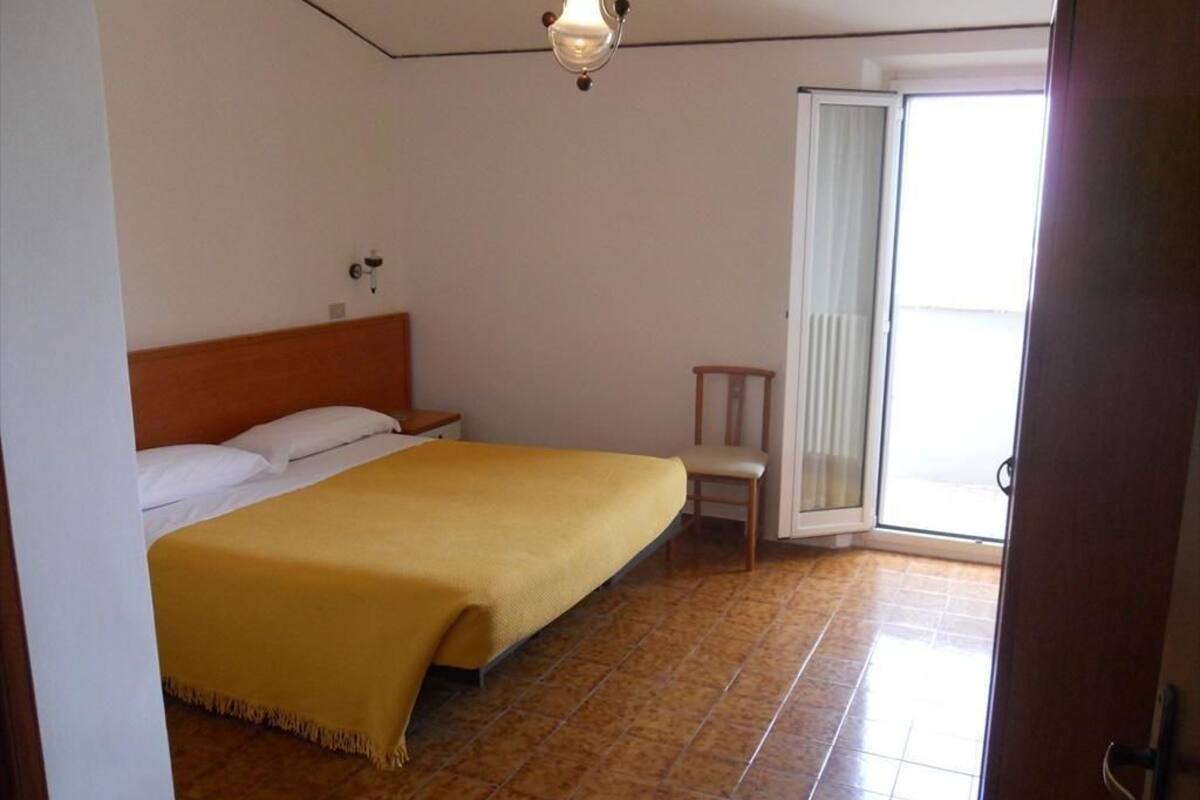 A bedroom with a bed, a nightstand, a chair, a window, and a door.