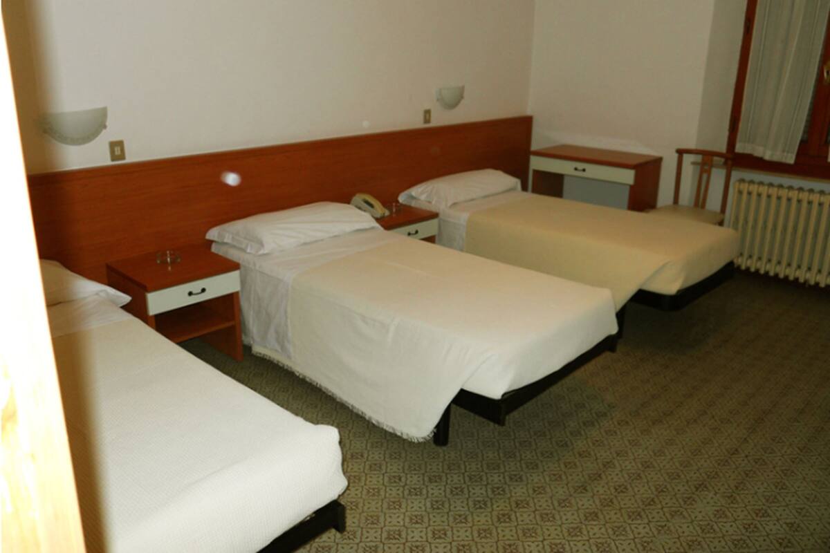 A hotel room with two single beds, a wooden headboard, bedside tables, a small desk, and a radiator.